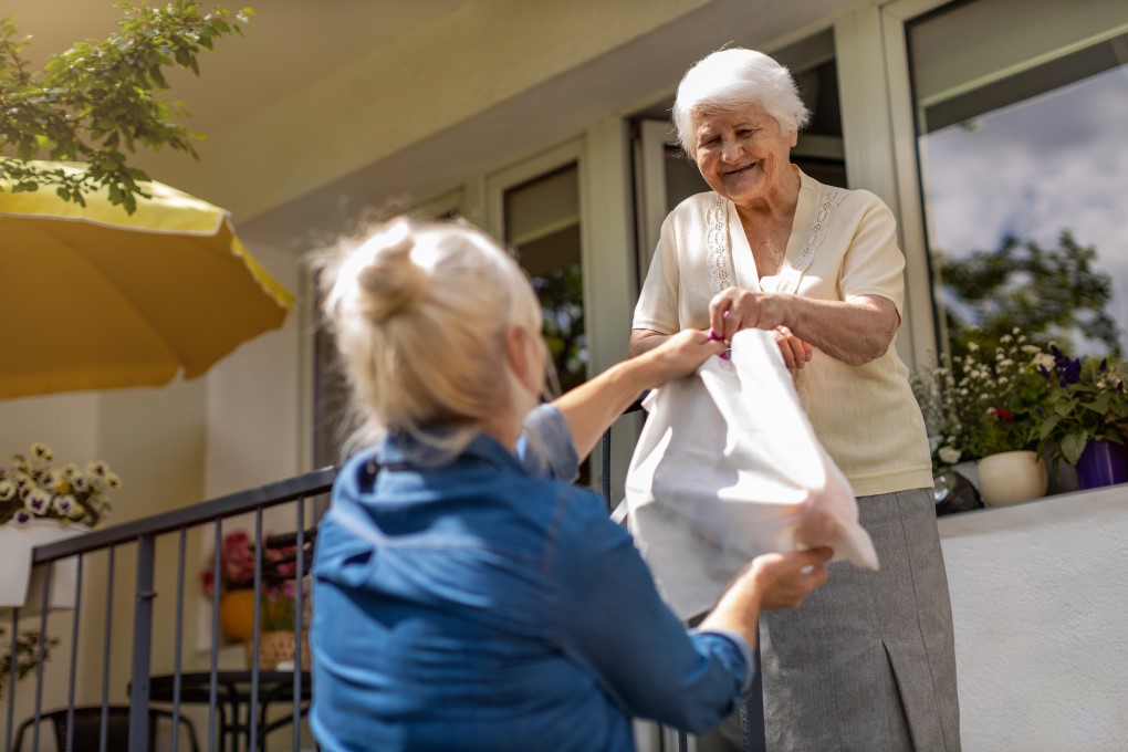 An older woman hands a bag to a younger woman, both smiling in a friendly exchange.