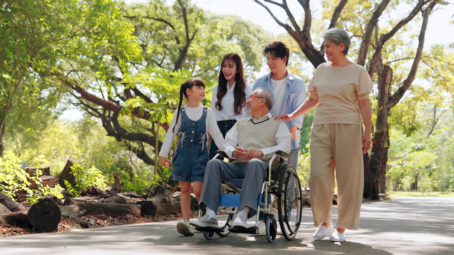 An elderly man in a wheelchair surrounded by his family, smiling and enjoying a moment together.