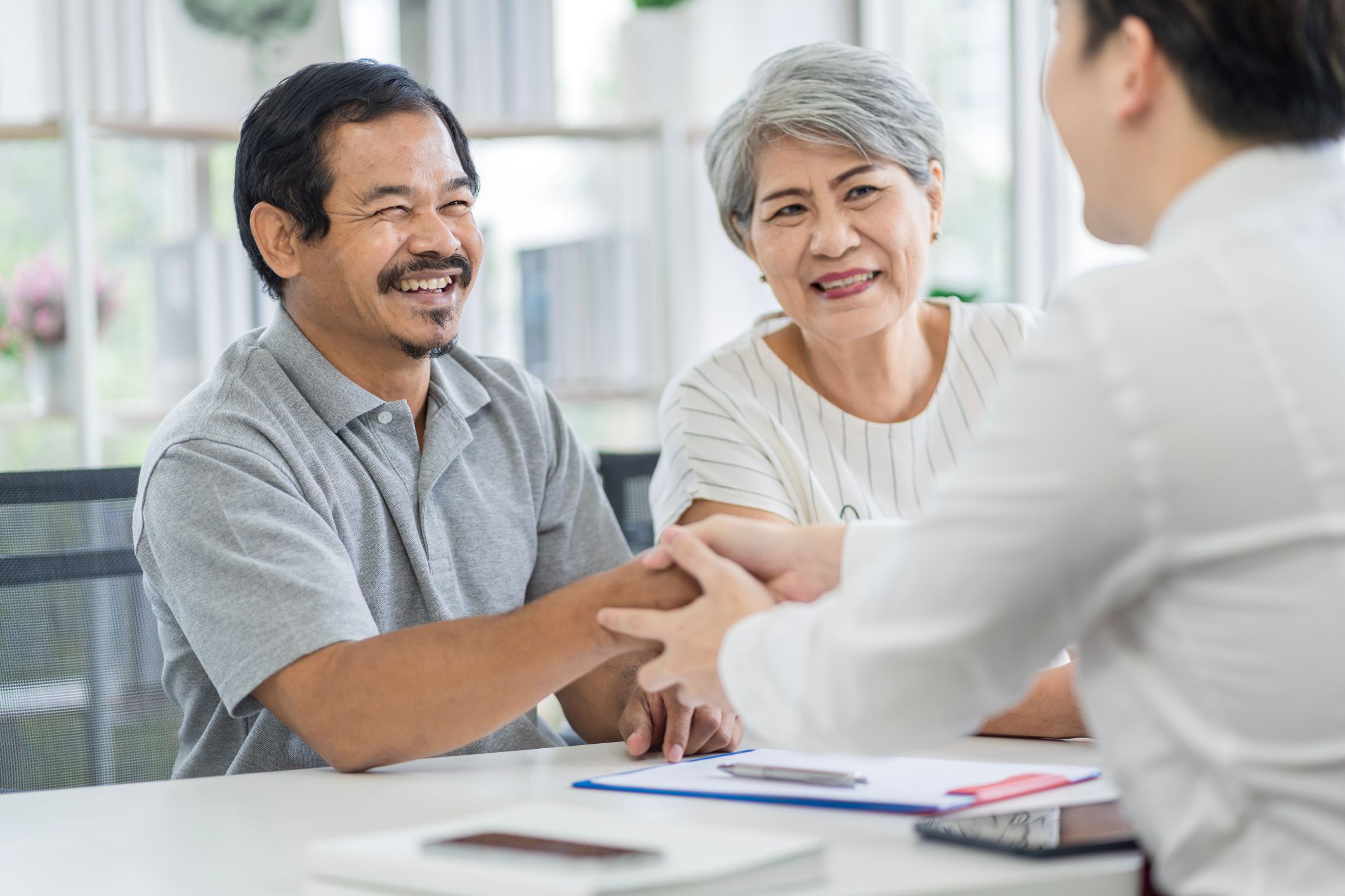 Asian couple discussing property options with a real estate agent in a modern office setting.