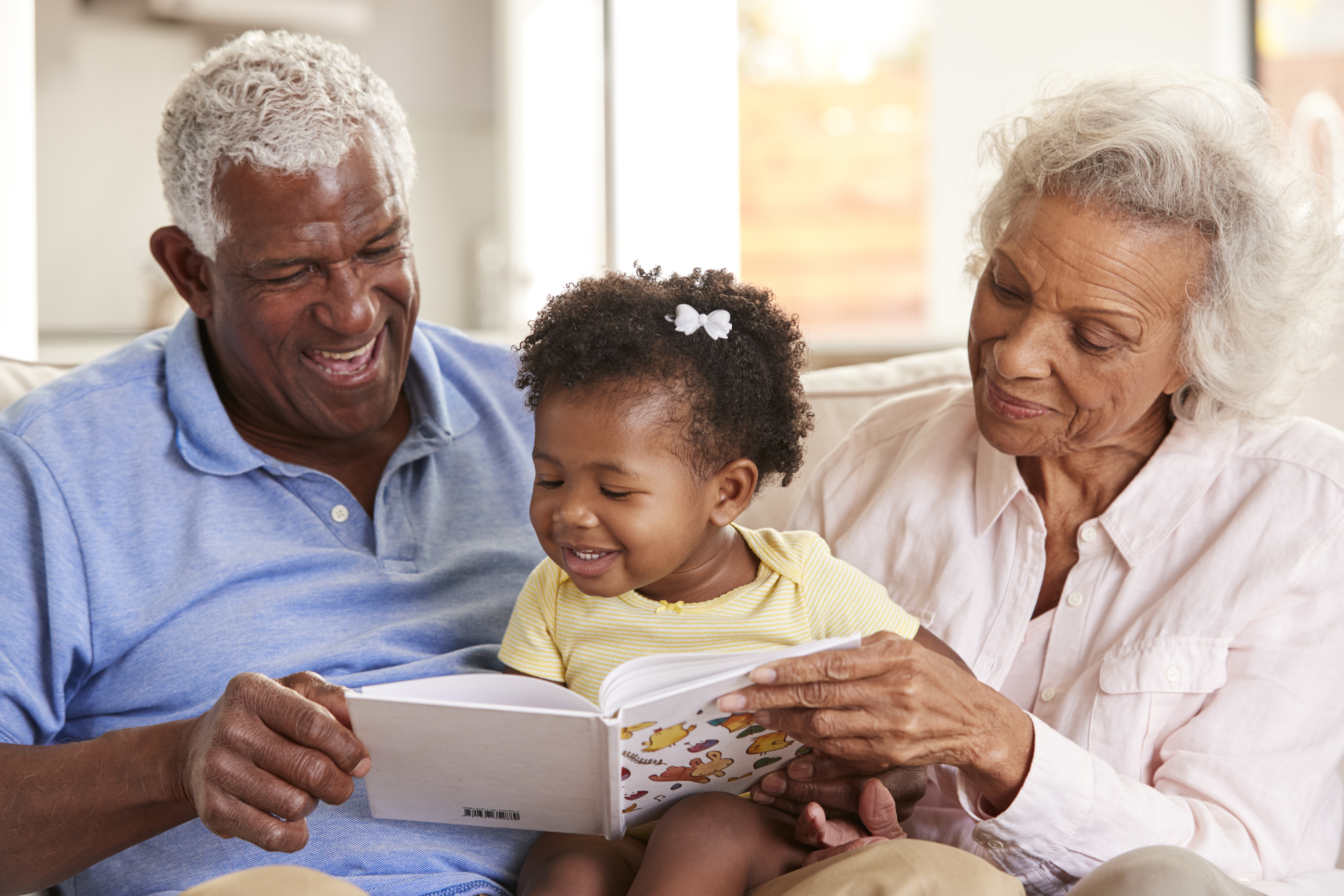 Older adult woman and man reading a children’s book to child on their lap, all smiling