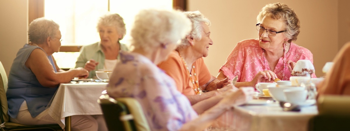 Elderly women eating and talking around a dinner table